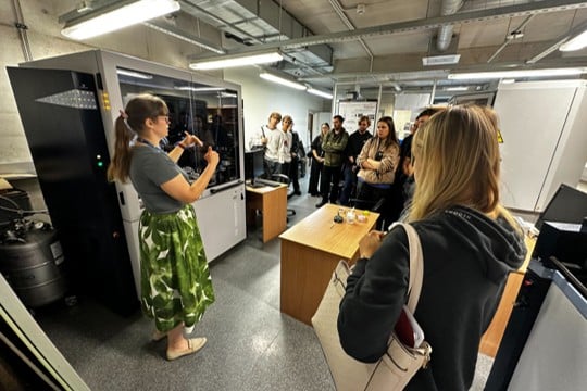 Cilvēku grupa klausās zinātnieces stastījumā