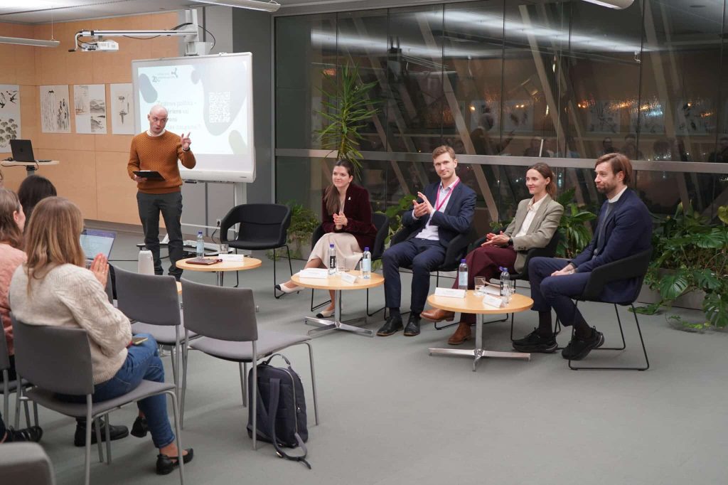 Diskusija LNB. Kājās stāv moderators, uz krēsliem sēž diskusijas dalībnieki